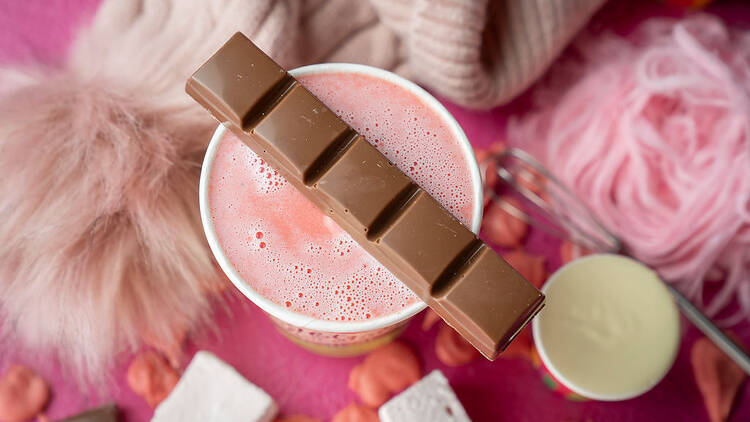 A pink hot chocolate with a bar of chocolate on top.