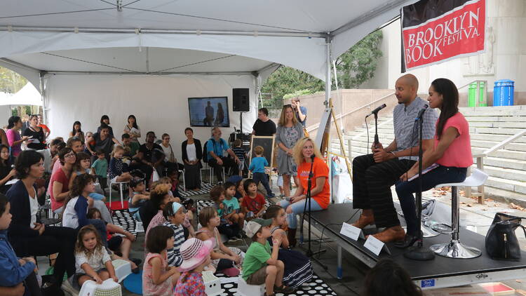 Two authors speak to a group of children.