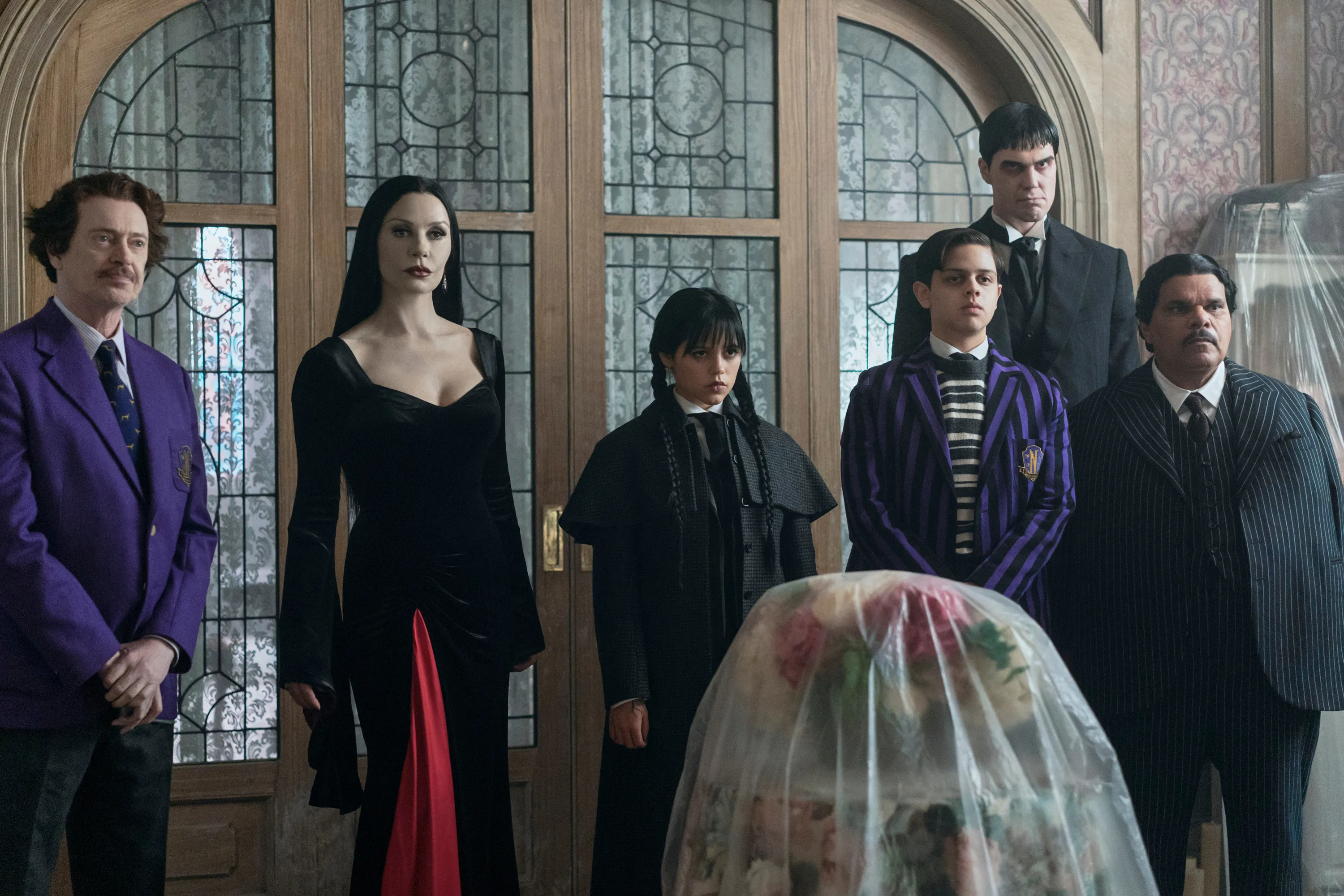 (L to R) Steve Buscemi as Barry Dort, Catherine Zeta-Jones as Morticia Addams, Jenna Ortega as Wednesday Addams, Isaac Ordonez as Pugsley Addams, Joonas Suotamo as Lurch, Luis Guzmán as Gomez Addams in Wednesday.