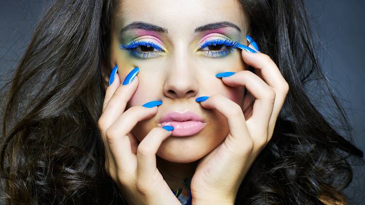 Photo of a young woman with bright makeup and blue manicure.