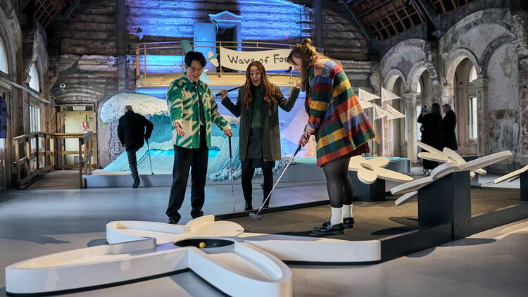 Three people playing mini golf.