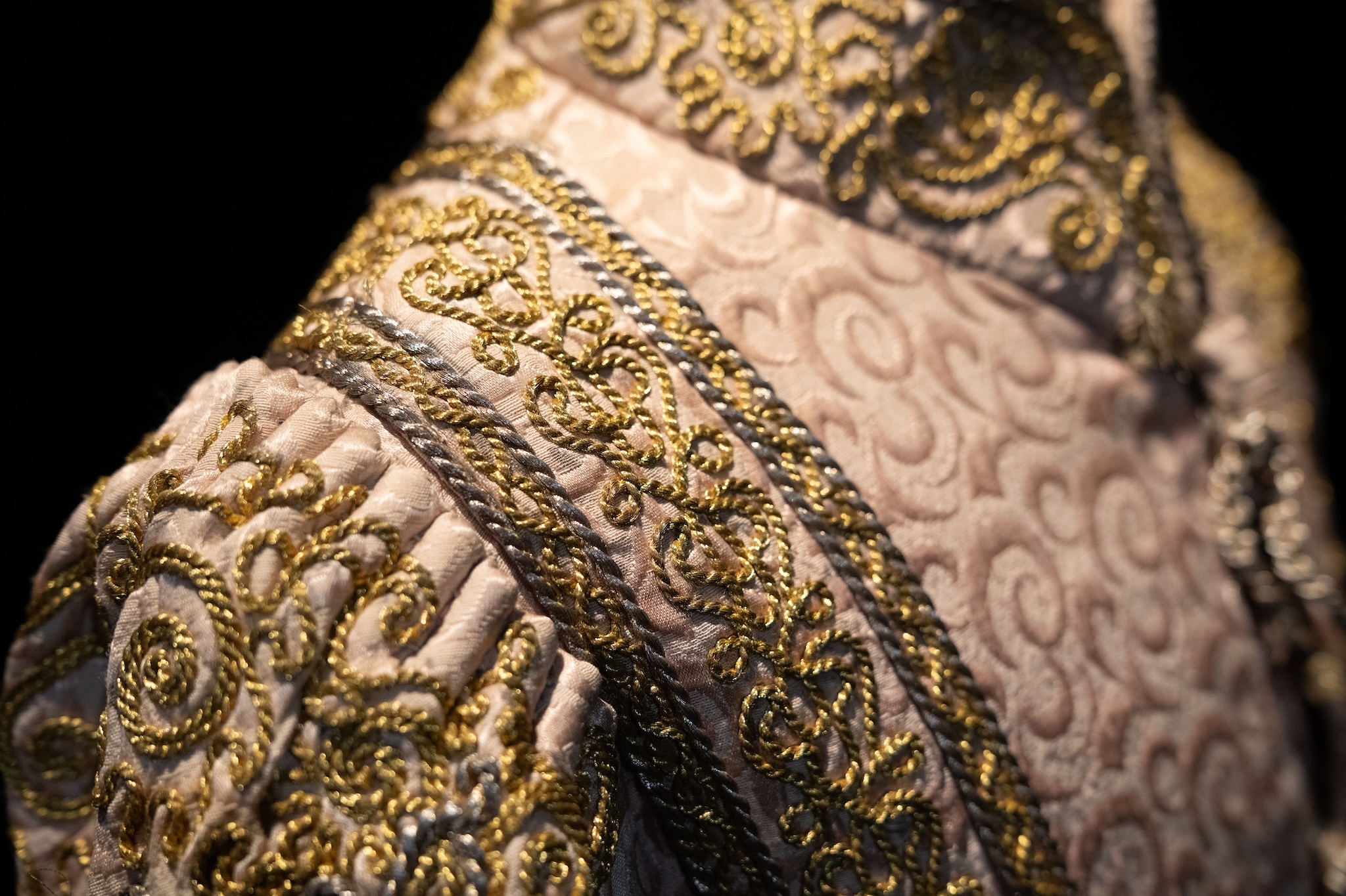 A close-up view of a costume with gold thread on a tan outfit.