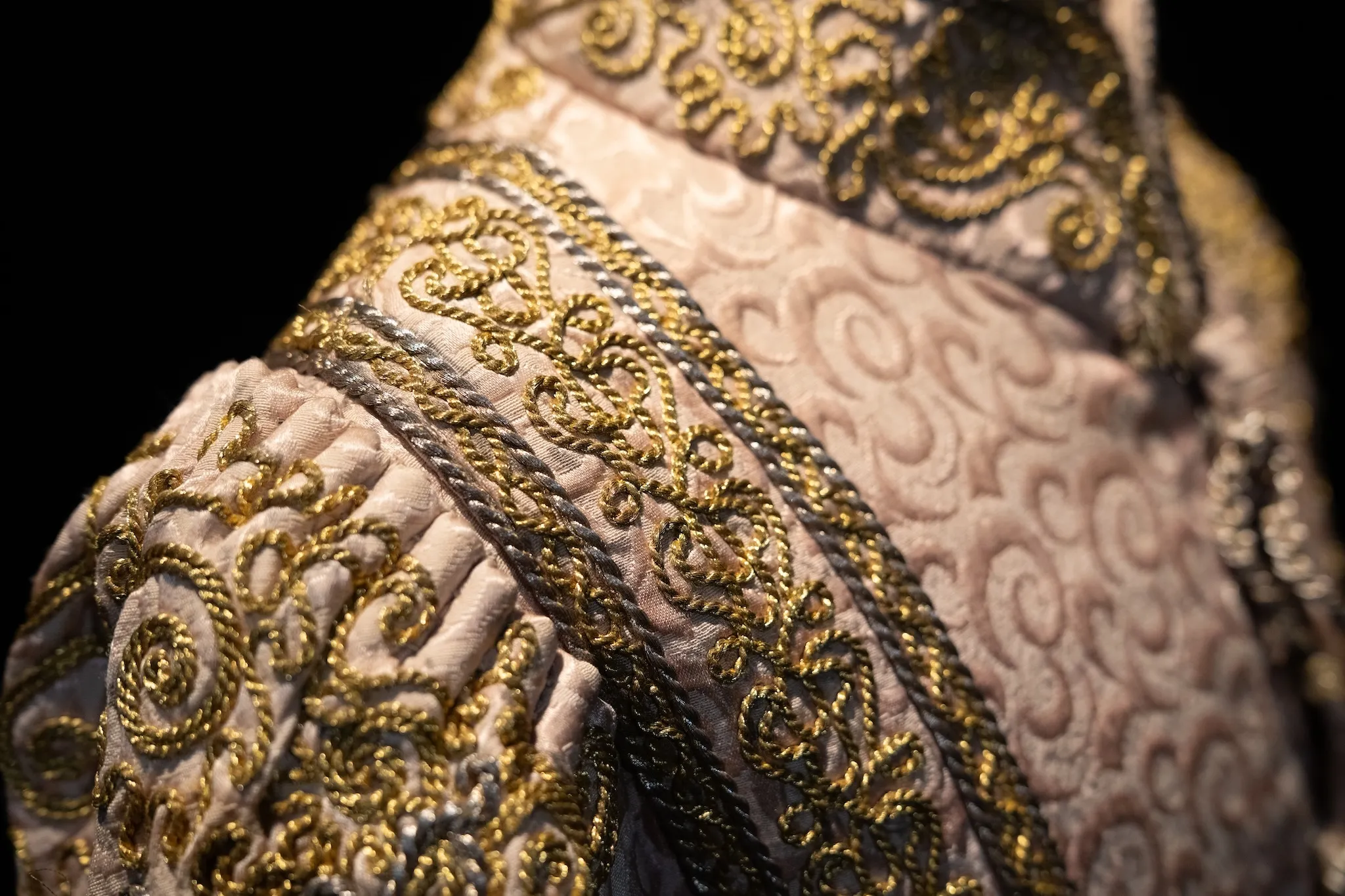 A close-up view of a costume with gold thread on a tan outfit.