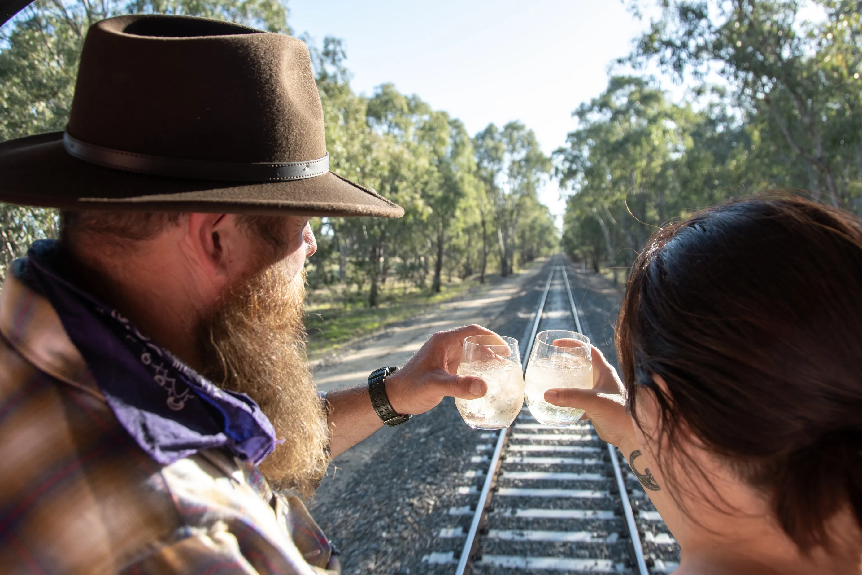 Two people clinking drinks overlooking train tracks.