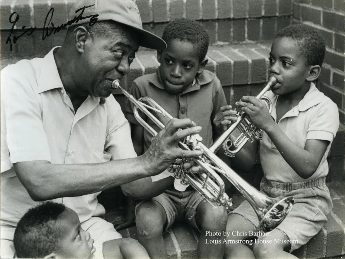 Three young boys sit on a staircase with Louis Armstrong learning to play the trumpet.