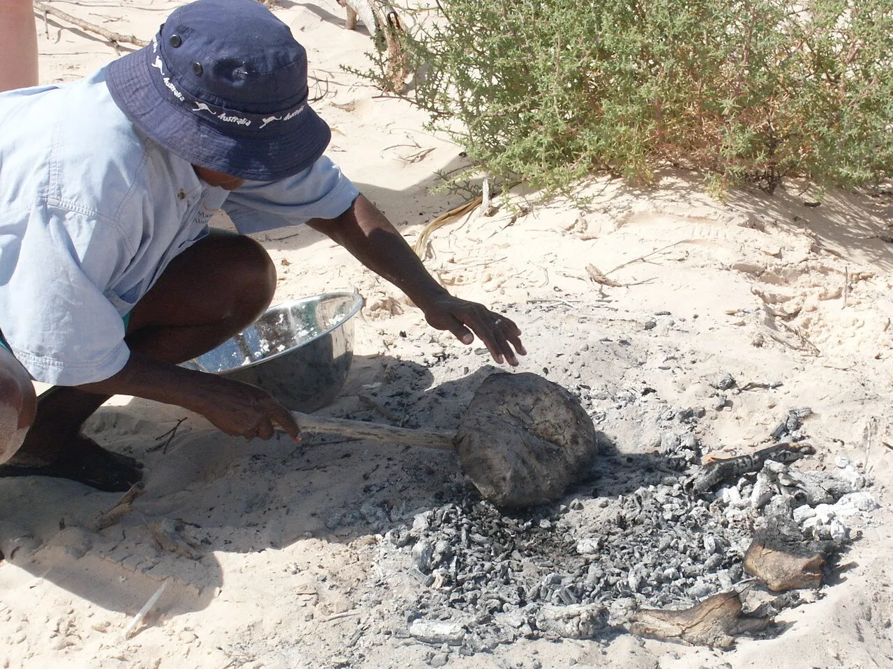Woman baking bread on coals in sand