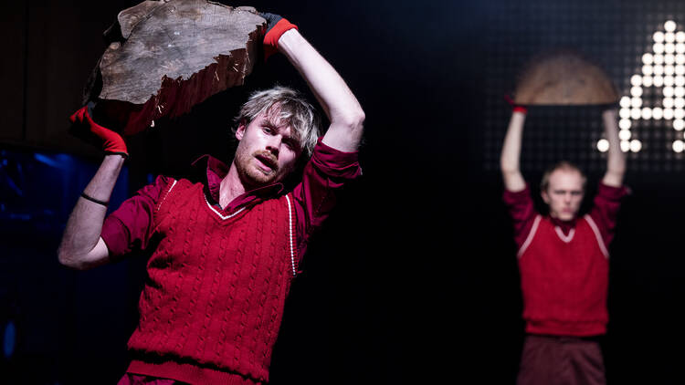 Two members of Pony Cam on stage during 'The Orchard' holding logs above their heads.