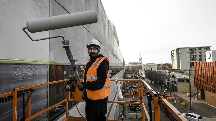 The artist Rone holding a paint roller on the site of the giant mural. 