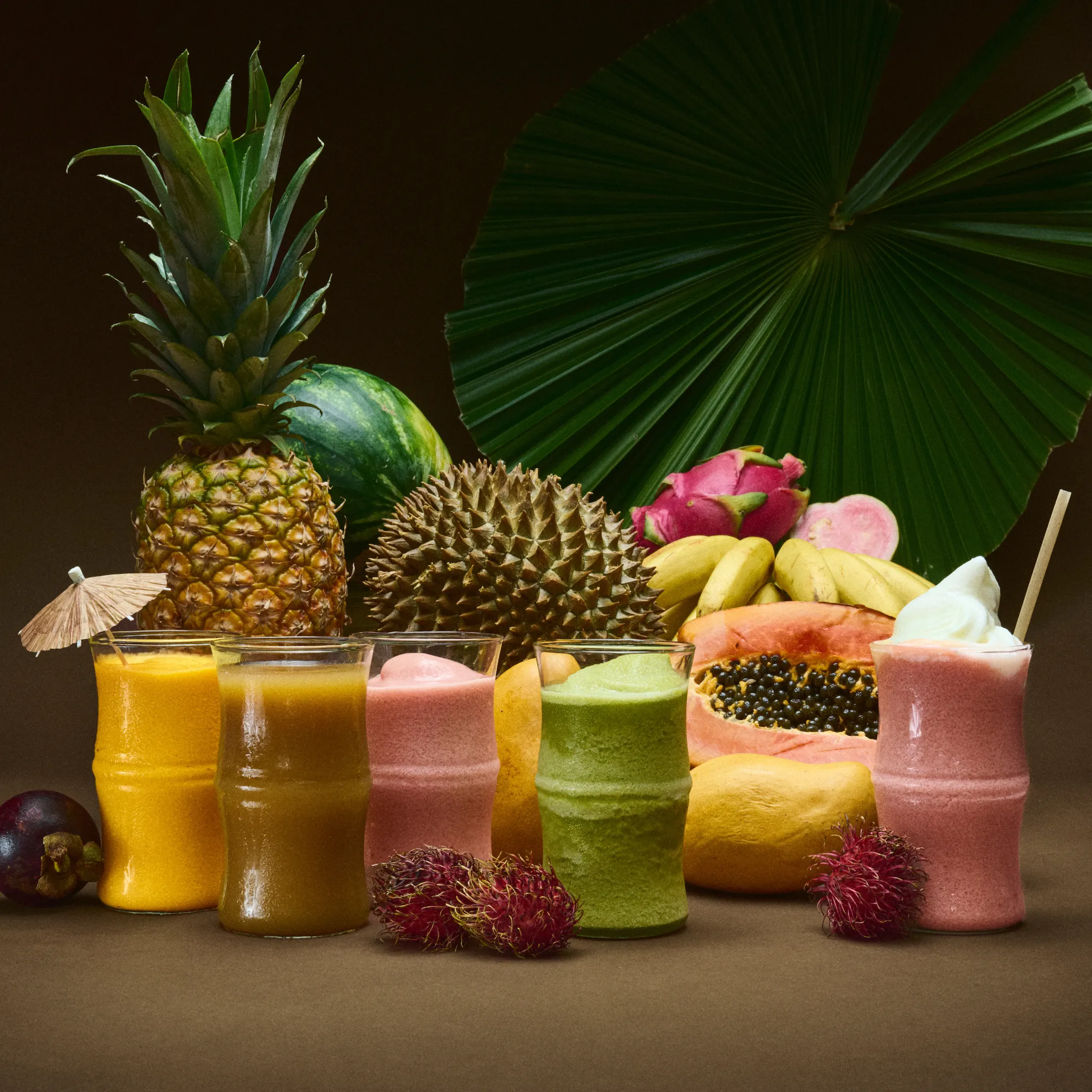 Frozen drinks in clear glasses with fruit behind it