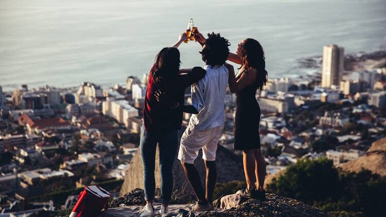 Group of friends toasting with beer bottles on scenic view over Cape Town