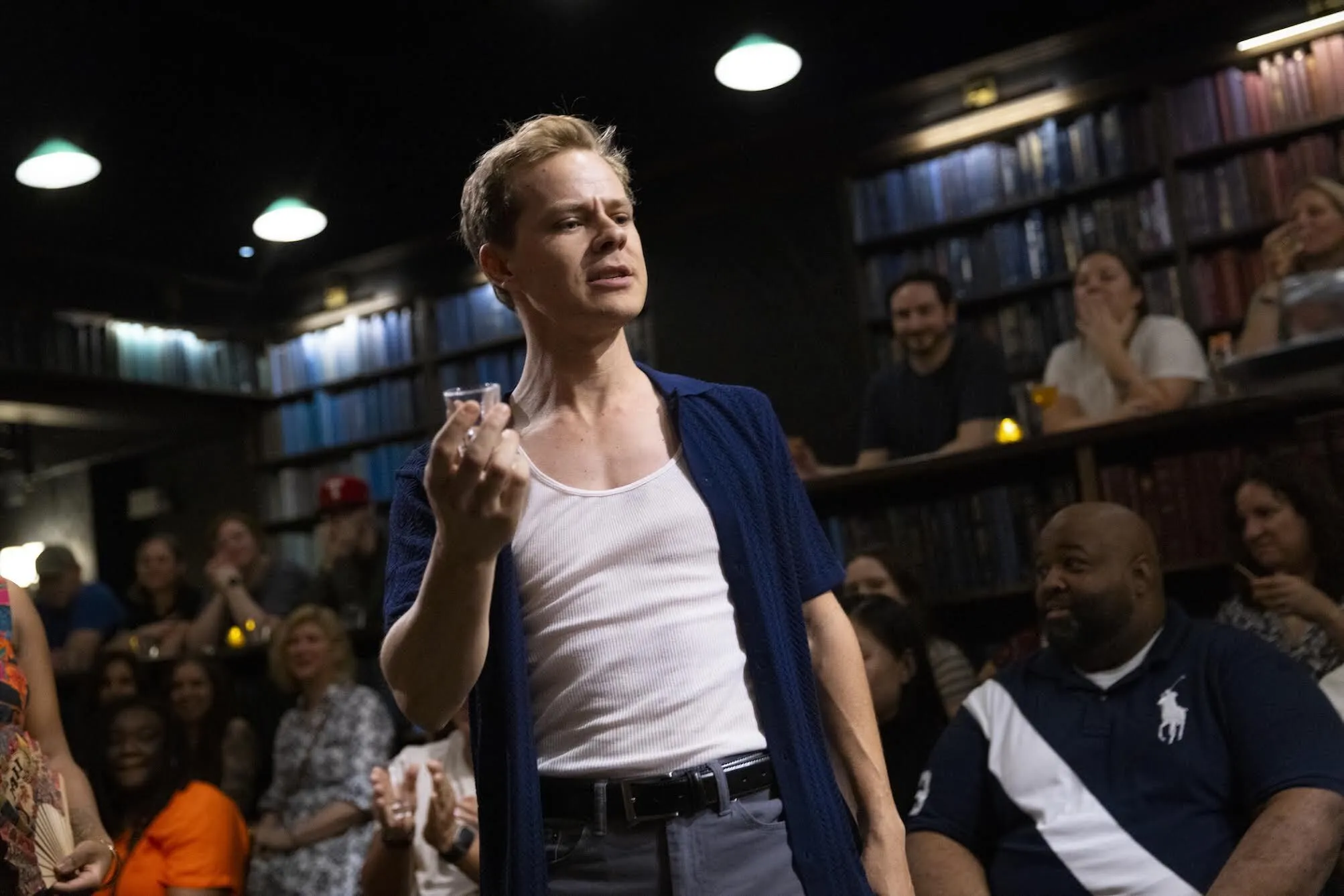 Actor Samuel Adams holding a shot glass in the middle of a performance with a delighted audience.