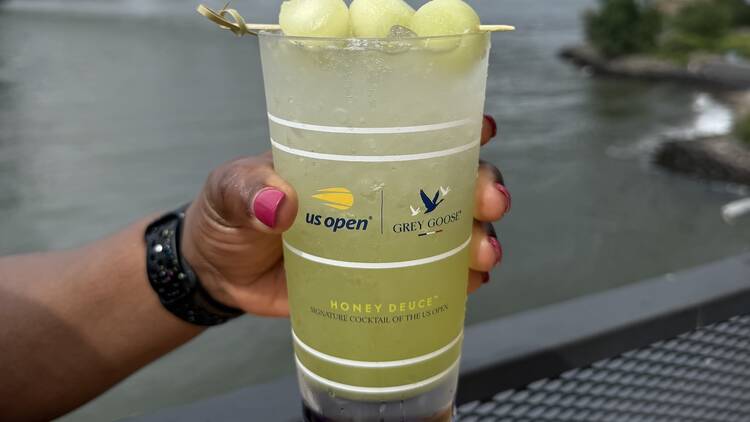 A green  Game Set Goose cocktail with the Manhattan bridge in the background