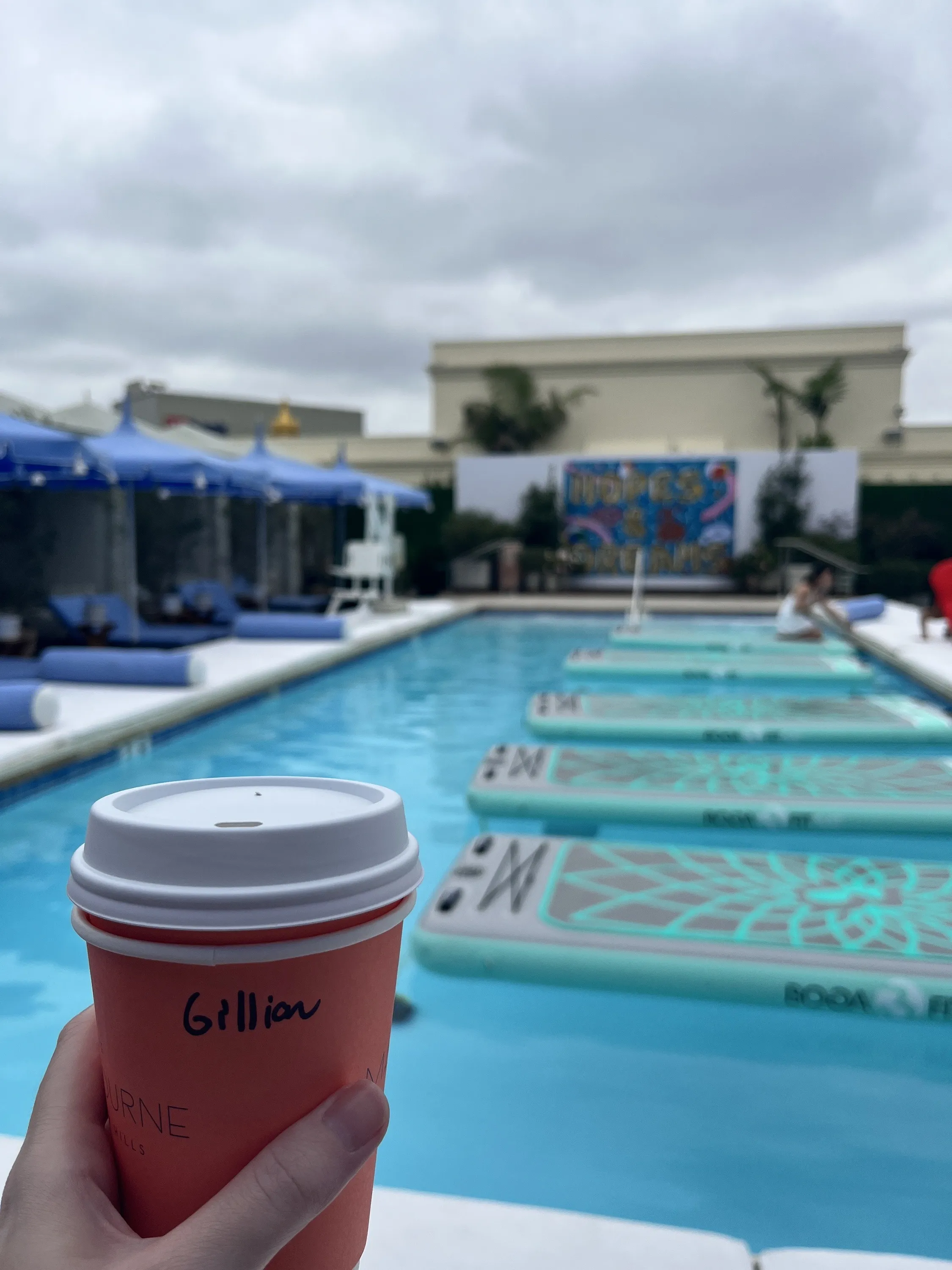 A coffee cup held in front of a rooftop pool.