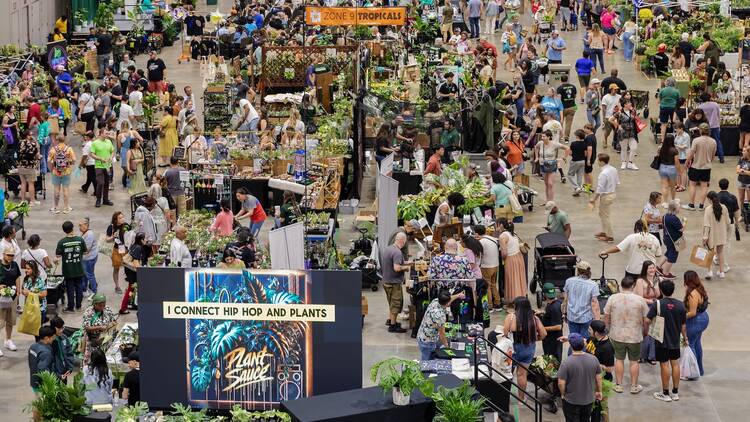 A large group of people in a convention space with tons of greenery and plants, as well as different booths set up to display them.
