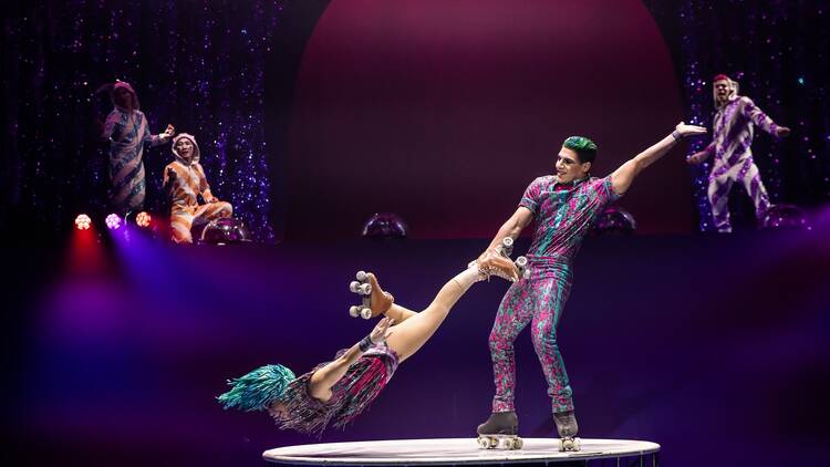Two roller skaters perform a trick atop a circular platform.