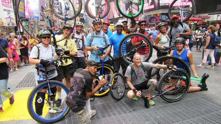 People gather in Times Square holding unicycles. 