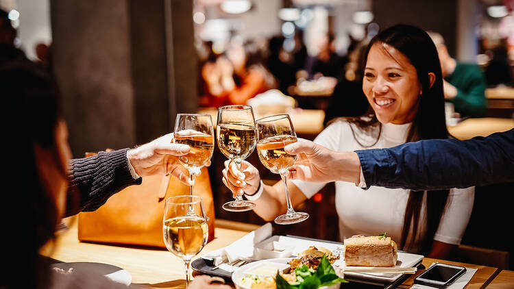Friends sitting at a restaurant table, raising wine glasses in a toast.
