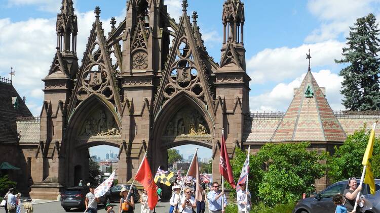 People carry flags outside of a Gothic arch inside Green-Wood Cemtery.