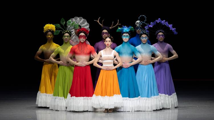 A group of dancers in technicolored costumes standing in an arc formation. A group of dancers in technicolored costumes standing in an arc formation.
