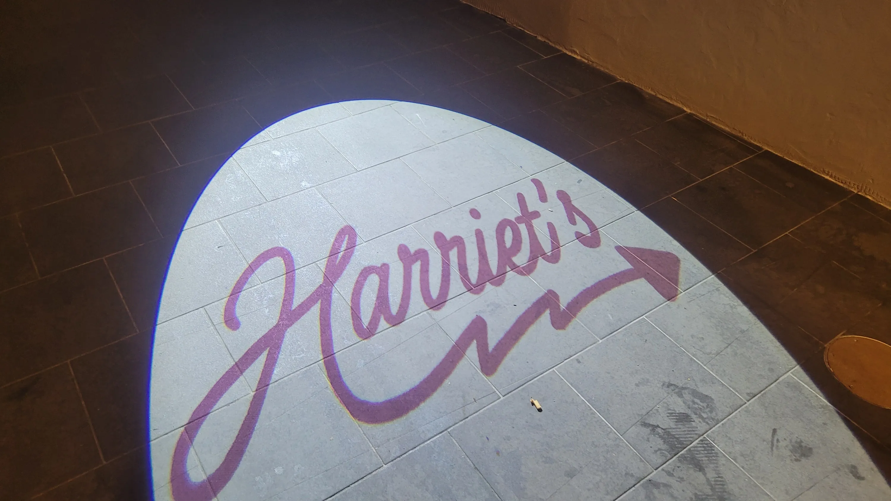 A light projection on the pavement that says 'Harriet's'