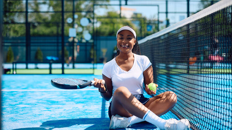 African American female paddle tennis player relaxing on the court and looking at camera. Copy space. 2156874373