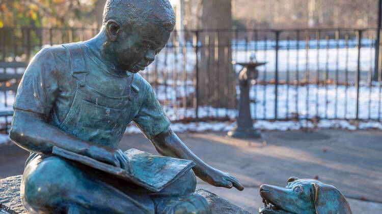 A statue of a boy and a dog sitting with a book while he pets the dog