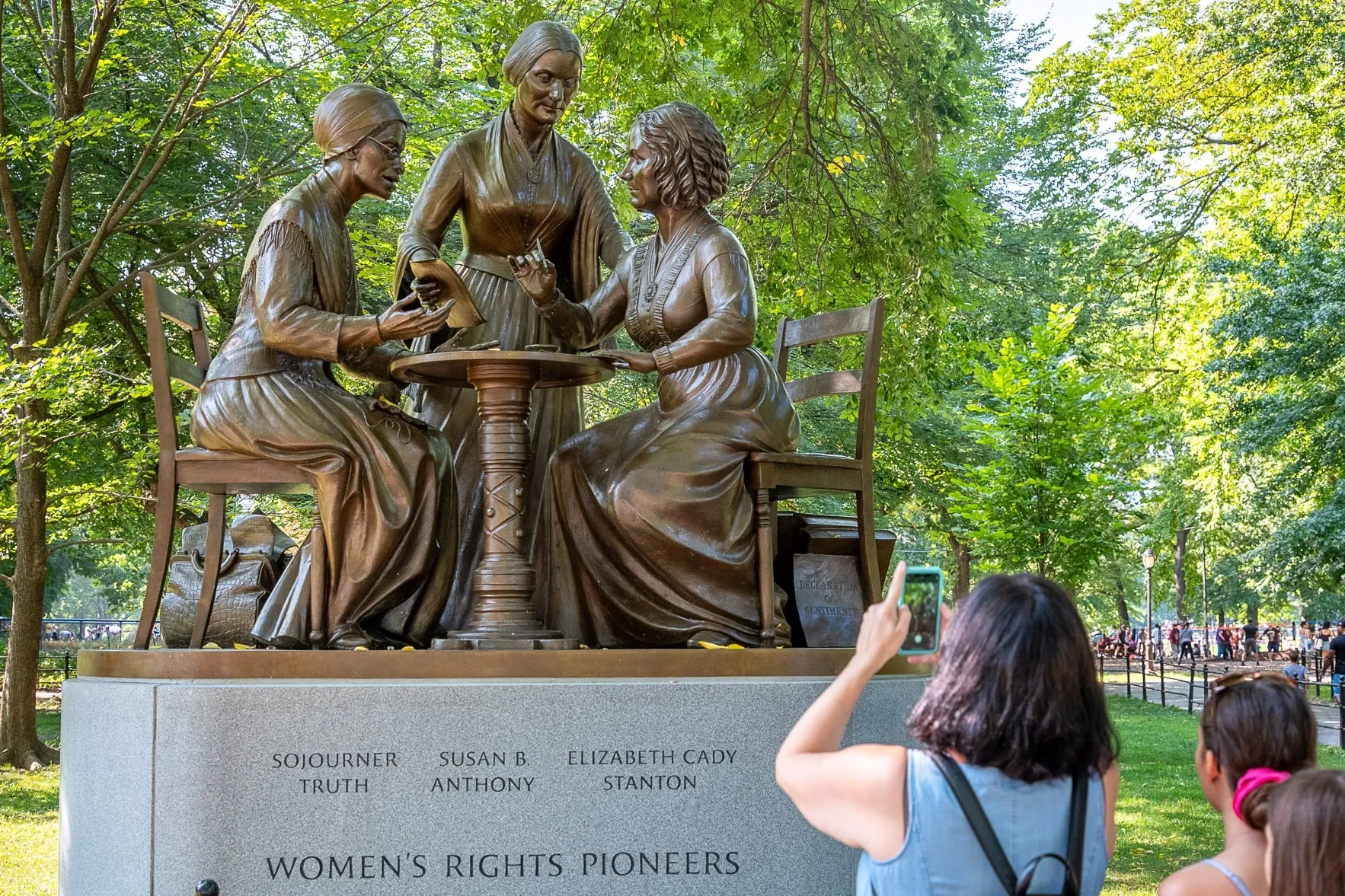 A statue of three women, two sitting down at a table and one standing up