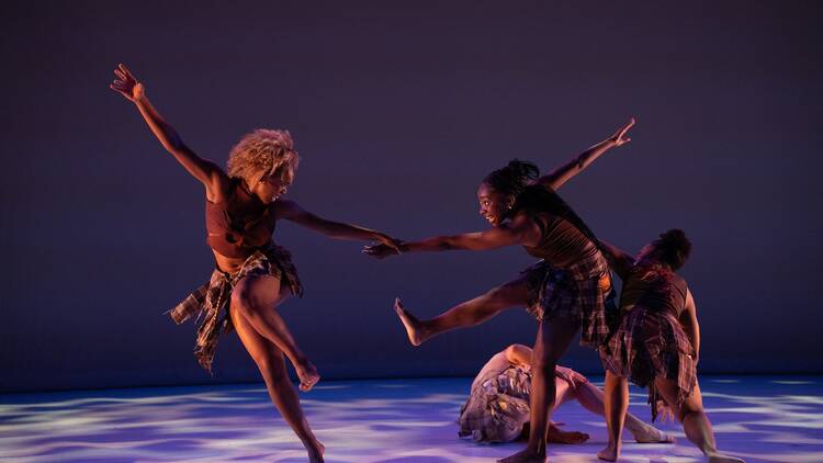 A group of dancers are pictured on a spotlit stage. 