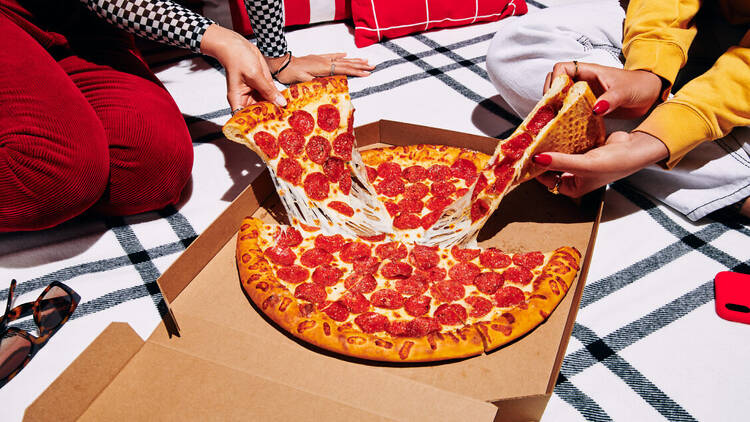 Two people eating a pepperoni pizza on the floor