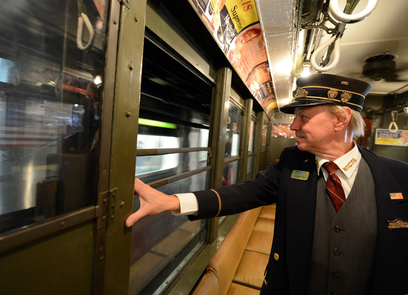 A train conductor on a vintage NYC subway standing up and holding onto the window