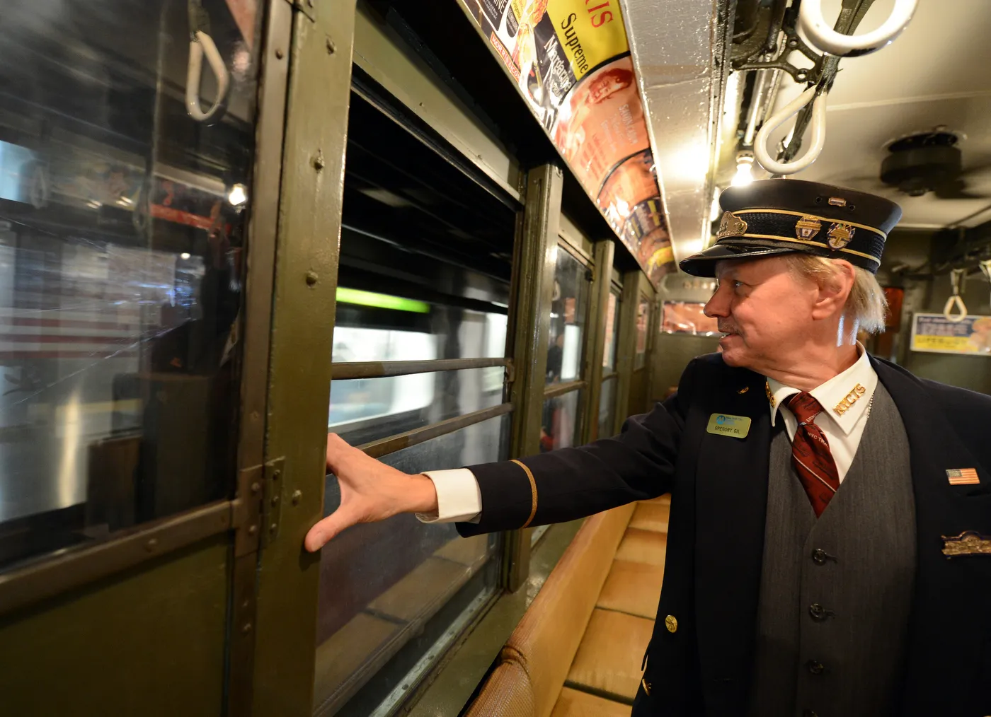 A train conductor on a vintage NYC subway standing up and holding onto the window