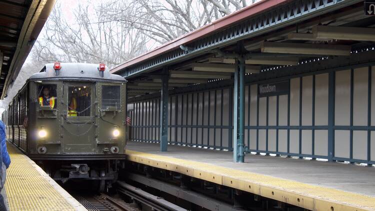 A vintage NYC subway train pulling into an outdoor station 