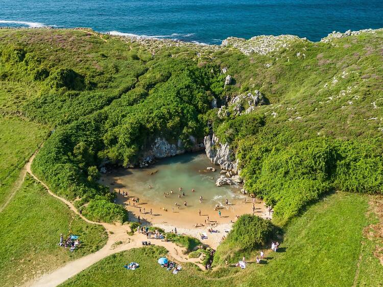 Gulpiyuri beach in Asturias, northern Spain. Aerial view of the unique Playa de Gulpiyuri, a hidden lagoon separated from the sea and surrounded by lush green meadows.