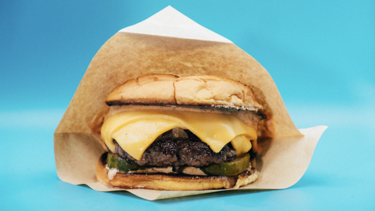 A close-up of a cheeseburger with a juicy beef patty, melted yellow cheese, and pickles, wrapped in parchment paper.