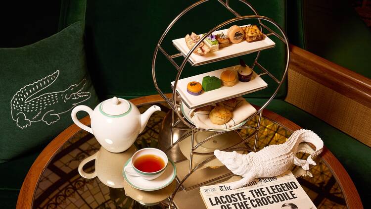 A silver tiered tray with a pot of tea and a white alligator on a glass table