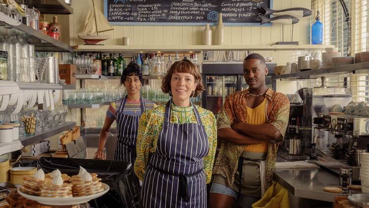 |  Olivia Colman (centre) with Sunita Amin (left) and Ncuti Gatwa (right) inside a seafood restaurant in The Roses