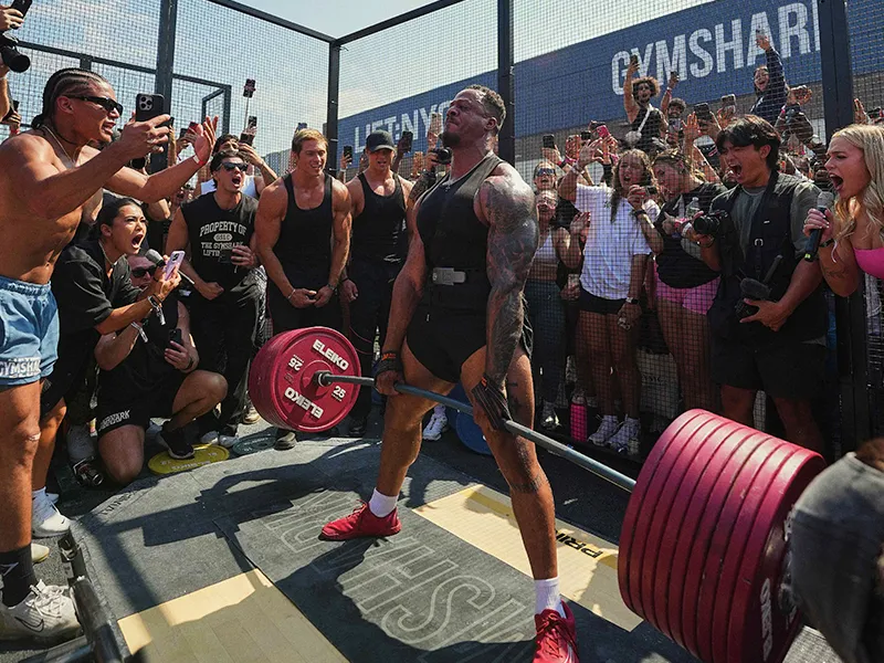 A bodybuilder deadlifts a barbell loaded with weights in a PR cage at at Gymshark event