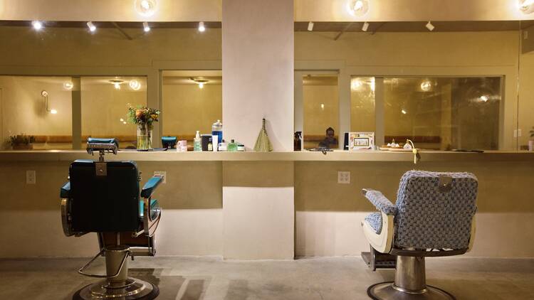 Two barbershop chairs in front of a large mirror