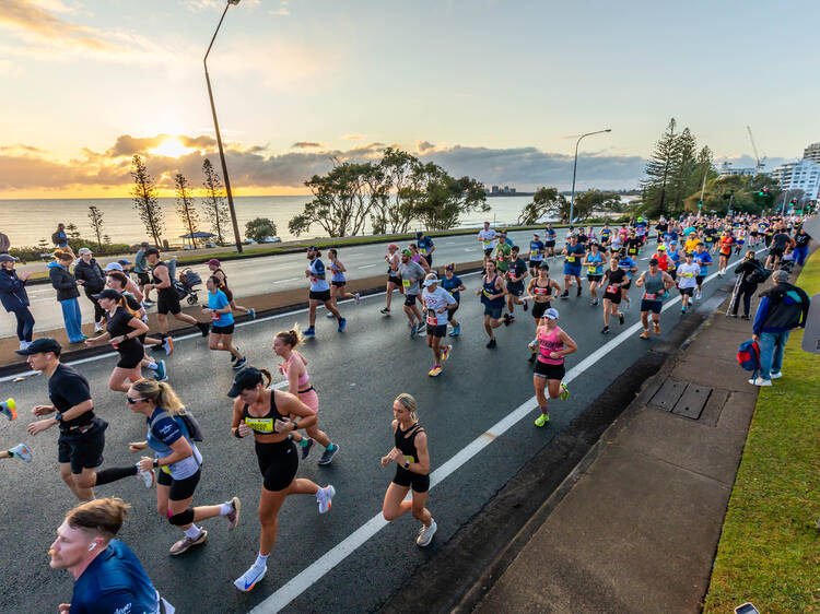 Runners on road next to water at sunrise