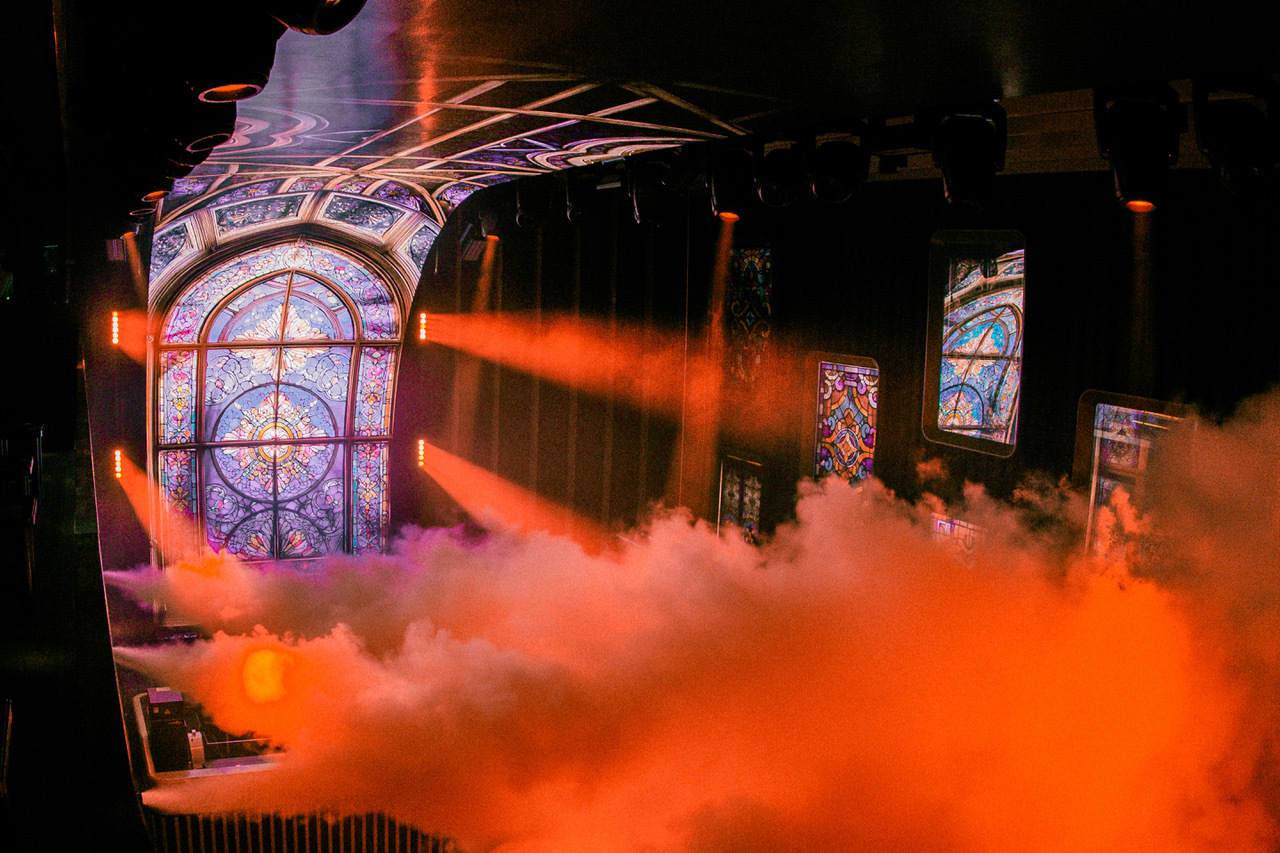 Nightclub with a colourful stained glass window and filled with smoke from dry ice jets 