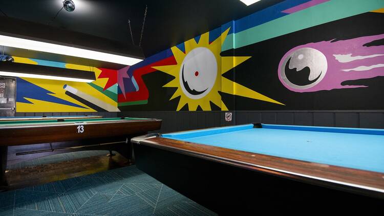 A cluster of pool tables placed in front of a colorful mural. A cluster of pool tables placed in front of a colorful mural.