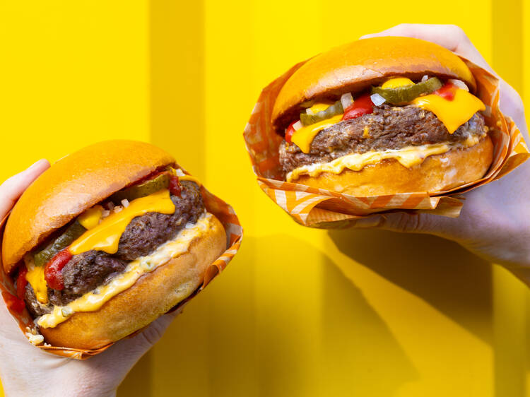 Zing Burger hamburgerek kézben tartva egy sárga fal előtt