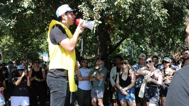 A person wearing a banana costume speaks into a microphone before a crowd of scavenger hunt competitors.