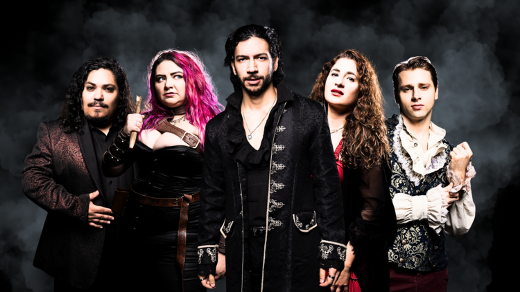 A group of five people dressed in Victorian garb stand in front of a smoky black backdrop.