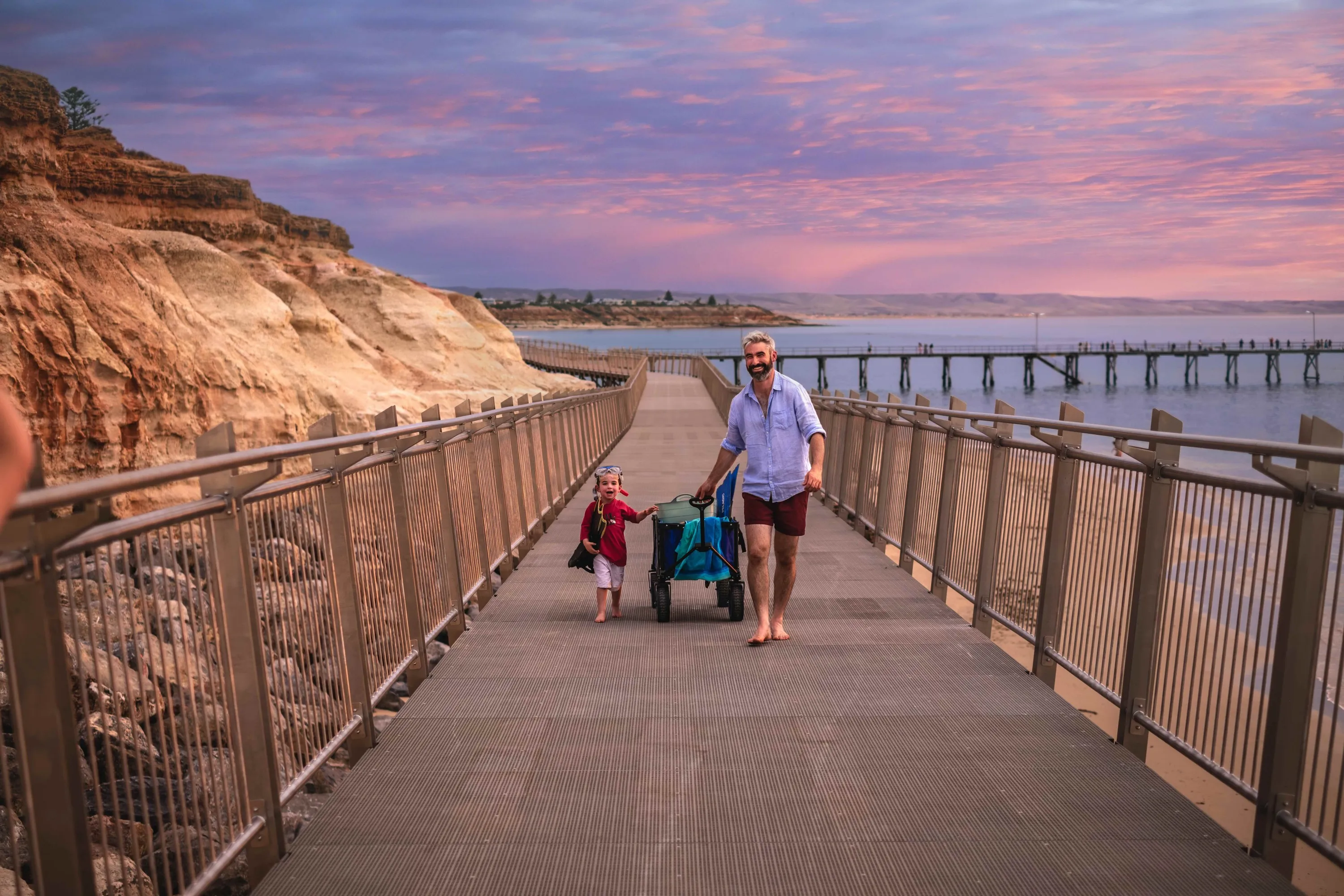 Man and kid walking on coastal track at sunset
