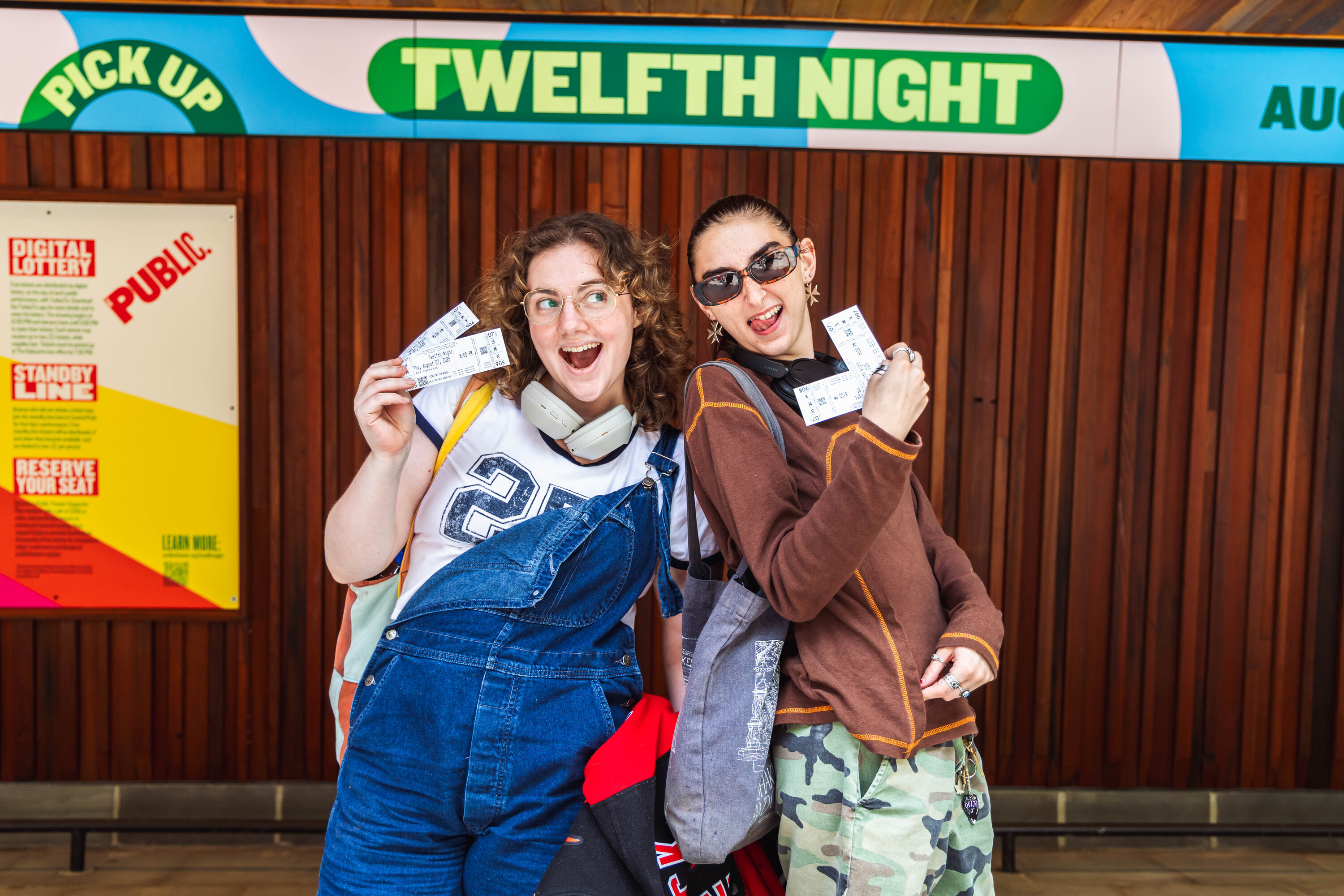 Two young women hold up their Shakespeare in the Park tickets.