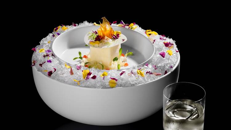 BarChef's Pina Colada cocktail seved with a large white bowl with flowers, ice and a square of sherbet 