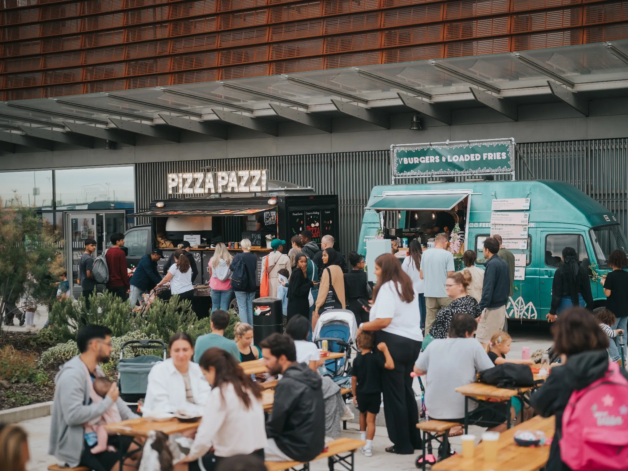 People sit on benches in front of a row of food trucks at Emerge East