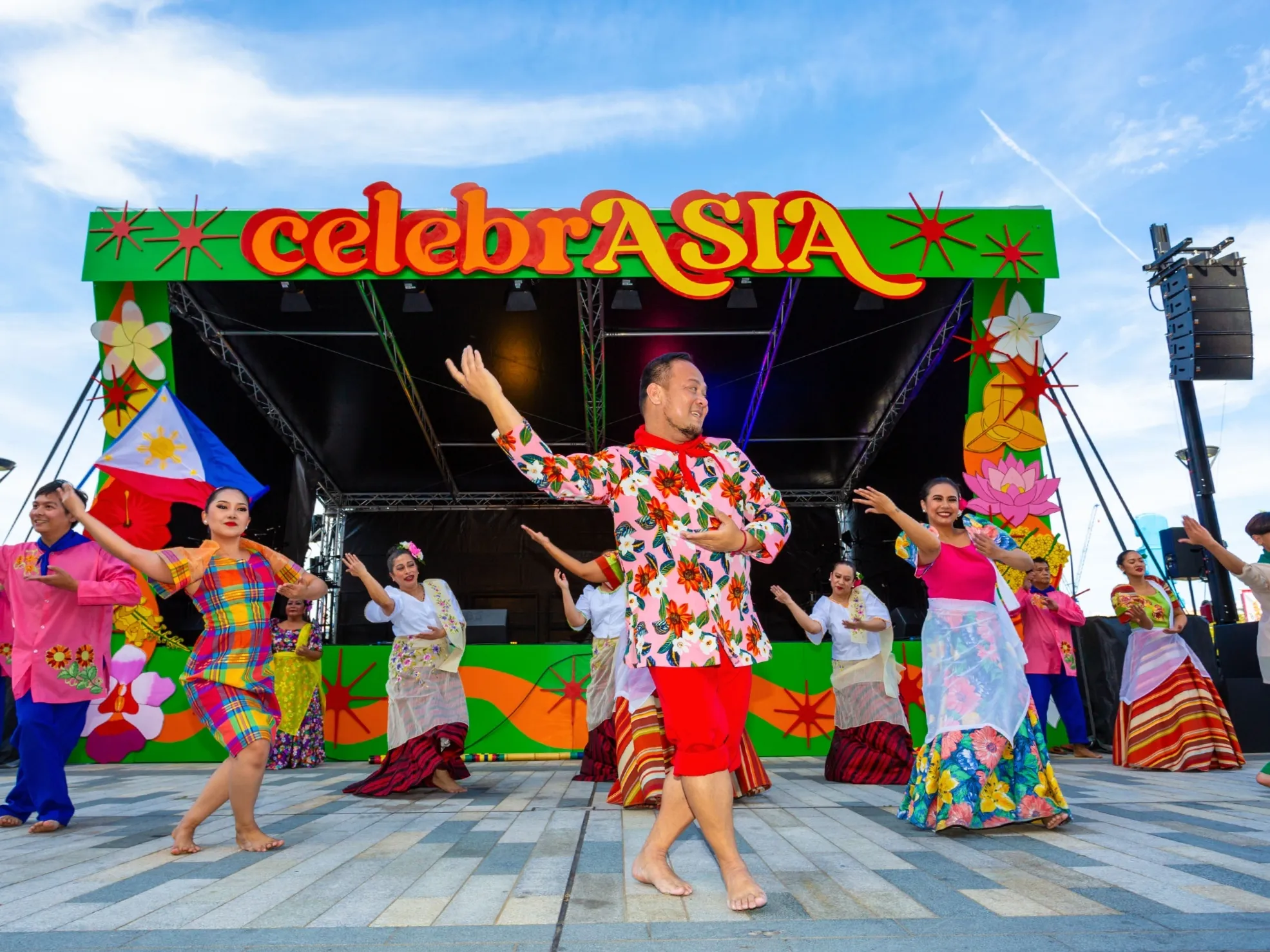 Traditional dancers wearing colourful costumes perform in front of a stage decorated with the ‘CelebrASIA’