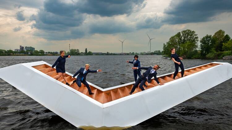 Five performers from Panama Pictures perform ‘The Weight of Water’ on an angular floating platform balancing on a lake